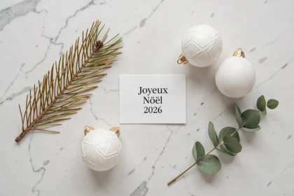 Composition minimaliste de Noël 2026 en vue du dessus avec branches de pin, boules blanches mates et carte Joyeux Noël sur marbre blanc